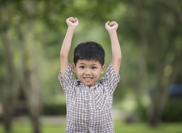 Little cute boy enjoying raising hands with nature over the blur