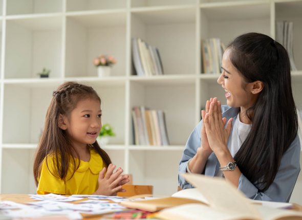 A caring Asian female teacher is clapping her hands with a little girl, feeling proud of her student